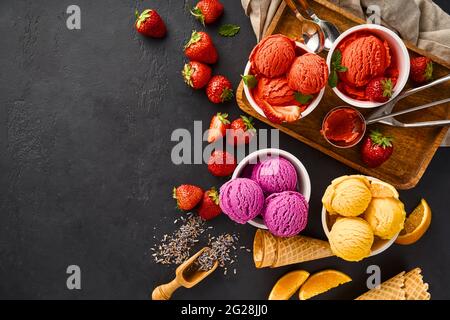 Tas de fraise et d'orange, lavande séchée avec des tasses de crème glacée. Sorbet lavande, fraise et orange sur fond noir avec espace de copie. Banque D'Images