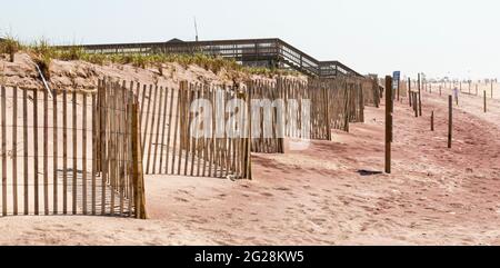 Clôtures de piquets de bois en face des dunes de sable avec une passerelle en bois au loin qui passe au-dessus des dunes sur les plages de la côte de la mer nationale des Îles-feu. Banque D'Images