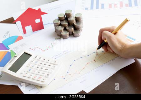 Tenez un stylo à la main et appuyez sur la calculatrice et le papier maison et les pièces de monnaie et le graphique de l'entreprise avec des lumières de soleil couleur tons arrière-plans Banque D'Images