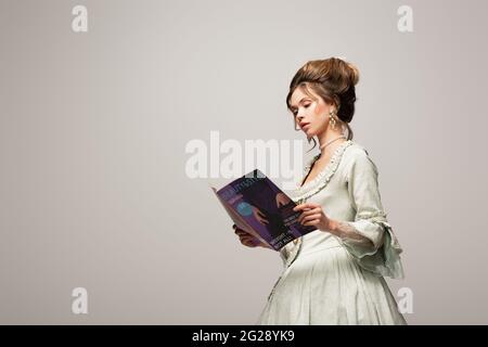 charmante femme en robe vintage lisant magazine moderne isolé sur gris Banque D'Images