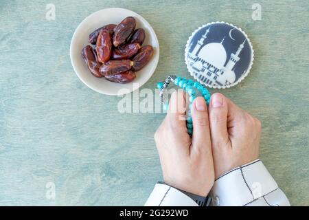 mains de femmes tenant le rosaire près des dates et le pain d'épice avec la mosquée. Fond de Kareem de Ramadan. Une femme musulmane vêtue de blanc tient un rosaire. Pose à plat. Banque D'Images