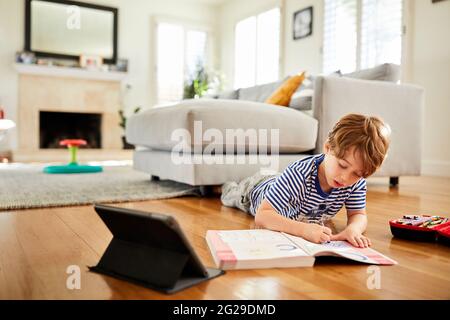 Coloriage de garçon dans un livre avec un crayon tout en apprenant en ligne à la maison Banque D'Images