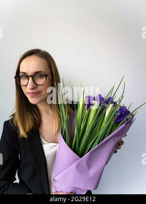 Jeune femme d'affaires avec des verres et un bouquet d'iris en veste noire Banque D'Images