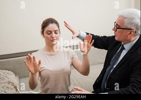 Homme mûr à cheveux gris hypnotises femme caucasienne pendant la séance d'hypnothérapie. Le psychologue utilise des traitements alternatifs pour l'esprit subconscient Banque D'Images