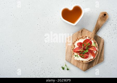 Gâteau au sarrasin croustillant sans gluten avec fromage à la crème, radis rouge, tomates et micro-vert pour un petit déjeuner sain sur fond de pierre grise. Voir fr Banque D'Images