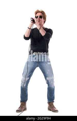 Jeune chanteur de rock passionné et énergique avec lunettes de soleil chantant sur le microphone. Longueur totale du corps isolée sur fond blanc. Banque D'Images