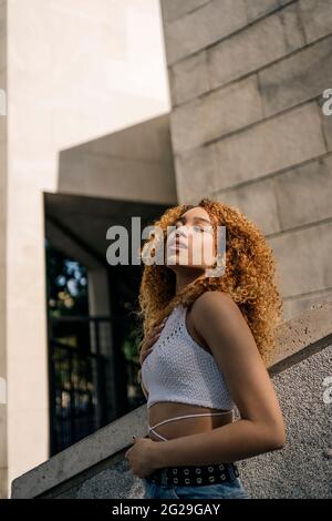 Photo de stock de portrait de jeune fille blonde courbeuse contre le mur. Elle a une attitude confiante. Elle porte des vêtements décontractés Banque D'Images