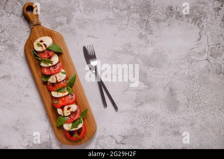 Salade de caprese italienne avec tomates en tranches, mozzarella, basilic, huile d'olive sur un plateau de service en bois. Banque D'Images