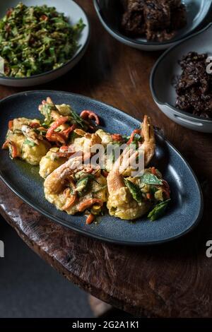 De dessus délicieux chaud grandes crevettes frites en pâte sur plaque ovale grise en composition avec des salades vertes et brunes floues sur table en bois Banque D'Images
