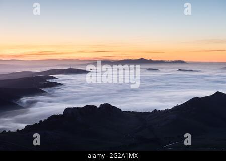 Vue aérienne du majestueux coucher de soleil calme au-dessus du brouillard nuageux dans la gamme des montagnes boisées Banque D'Images