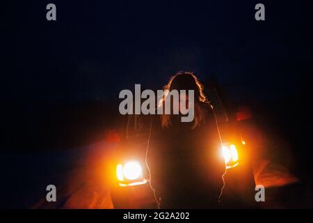 Femme voyageur debout devant la voiture avec des phares lumineux pendant le voyage dans la campagne enneigée la nuit en Islande Banque D'Images