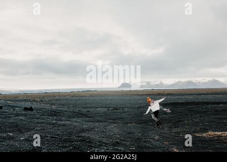 Vue arrière d'une jeune fille avec bras étirés sur une surface rocheuse le jour nuageux dans la campagne islandaise Banque D'Images