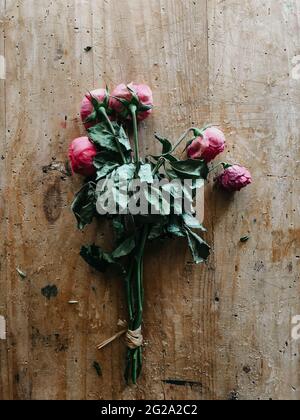 De dessus bouquet de fleurs Ranunculus rose nouées avec de longues tiges et des feuilles vertes sèches sur une table en bois sorbrée Banque D'Images