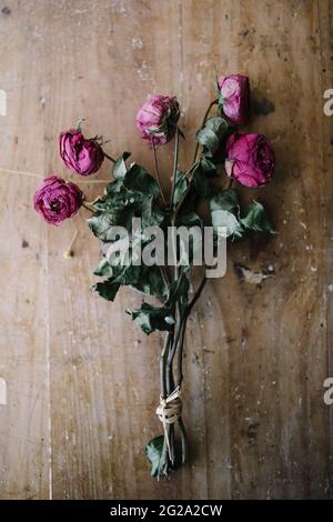 De dessus bouquet de fleurs Ranunculus rose nouées avec de longues tiges et des feuilles vertes sèches sur une table en bois sorbrée Banque D'Images