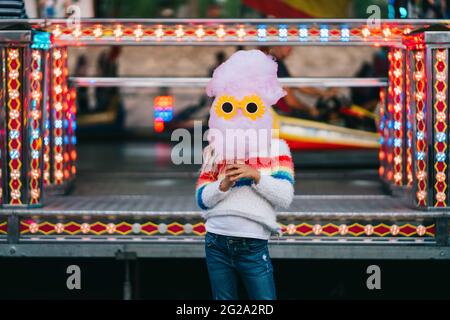 Petite fille tenant un bonbon de coton avec des lunettes de soleil drôles devant son visage Banque D'Images