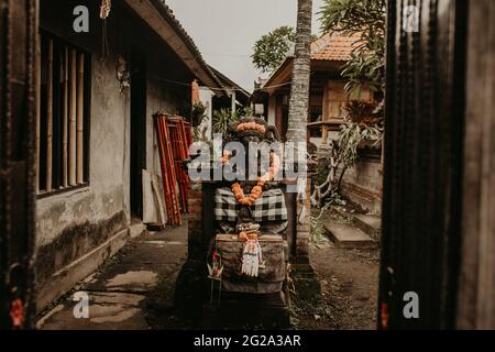 Petite idole religieuse traditionnelle décorée de fleurs sur une cour exotique paisible Banque D'Images