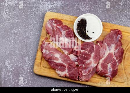 Steak de lame cru de l'épaule de porc sur une planche de bois sur un fond en bois foncé. Vue de dessus, plan d'appartement Banque D'Images