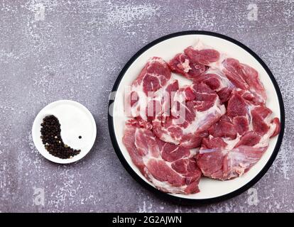 Steak de bœuf cru de l'épaule de porc dans une assiette blanche sur un fond en bois foncé. Vue de dessus, plan d'appartement Banque D'Images