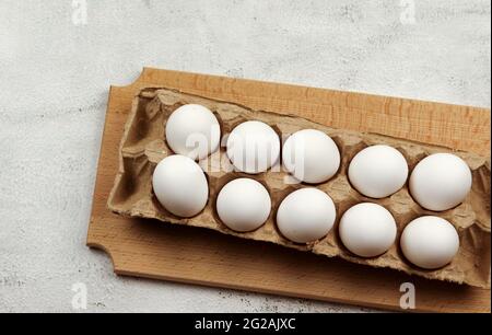 Œufs de poulet blanc crus dans une cassette sur une planche à découper en bois sur fond gris clair. Vue de dessus, plan d'appartement Banque D'Images