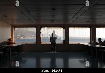 Détroit de Messina, Italie - 05 juillet 2010 : vue arrière d'un homme debout et regardant la côte depuis la grande fenêtre du ferry, d'autres passagers assis moi Banque D'Images