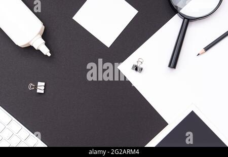 Maquette de lieu de travail dans des tons noirs et blancs contrastés. Bureau avec papeterie, livre, feuille vierge, loupe, clavier et crayon. Vue de dessus, espace pour Banque D'Images