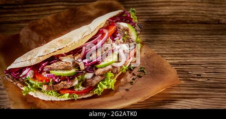 Grand angle de délicieux kebab de doner en pita avec de la viande et des légumes placés sur une table en bois Banque D'Images