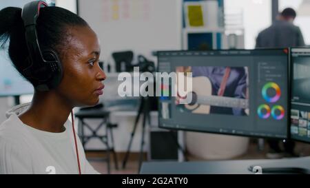 Belle femme africaine vidéaste avec casque montage vidéo sur pc avec deux écrans travaillant dans l'agence de création. Employé utilisant un logiciel de post-production travaillant dans un bureau d'agence de création. Banque D'Images