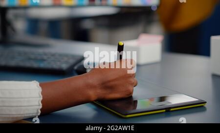 Gros plan sur l'éditeur de photo africain dessin sur tablette graphique retouche photo client sur ordinateur avec deux moniteurs. Retouche noire tenant un stylet pour retoucher des documents dans un bureau d'agence de création Banque D'Images