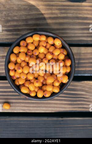 Baies d'argousier mûres d'orange juteuse dans un bol sur une table en bois, vue du dessus. Fruits du travail agricole. Ingrédients pour plats. Baies pour la congélation. Banque D'Images