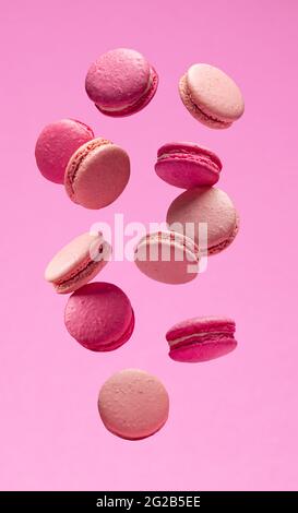 Macarons doux colorés ou macarons, biscuits aromatisés flottant dans l'air sur fond rose. Banque D'Images