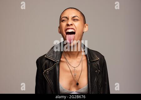 Portrait d'une femme androgyne portant une veste en cuir noir. Femme avec la tête rasée qui dépasse la langue et regarde loin. Banque D'Images