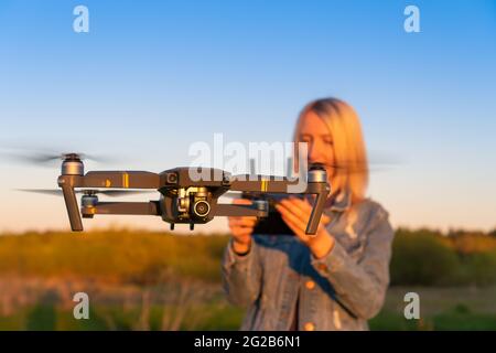 Une jeune femme blonde contrôle un drone dans la nature pendant le coucher du soleil. Au premier plan se trouve un drone de gros plan Banque D'Images