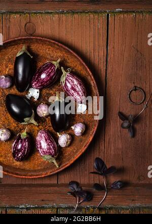 Petits légumes d'aubergine ou d'aubergine à l'ail et feuilles de basilic violets sur fond de bois rustique ancien. Concept de nourriture saine avec espace de copie. Banque D'Images