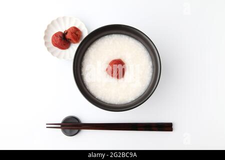 porridge de riz avec prune marinée au sel dans des baguettes de bol isolées sur fond blanc Banque D'Images