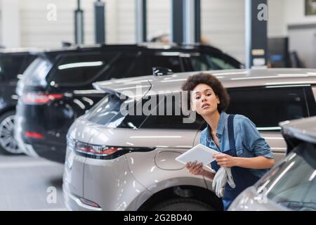 un jeune mécanicien afro-américain vérifie les voitures avec une tablette numérique dans un garage Banque D'Images