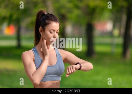 Concept de mode de vie sain - la femme vérifie son pouls après l'entraînement de jogging dans le parc. Le concept d'un mode de vie sain et de maintien en forme dans une forme de merde Banque D'Images
