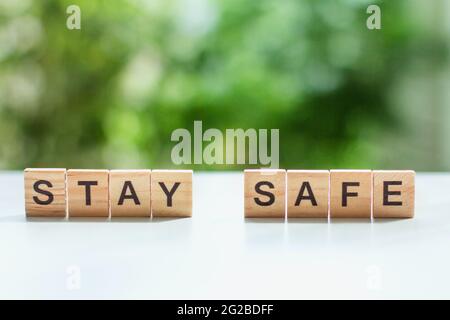 Mot rester en sécurité message signe de cubes en bois sur une table lumineuse sur un fond de feuilles vertes dans le foyer doux social distanciation, concept restant à Banque D'Images