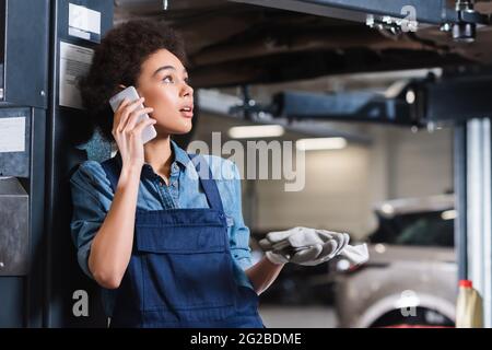 inquiet jeune mécanicien afro-américain parlant au téléphone portable dans un garage Banque D'Images