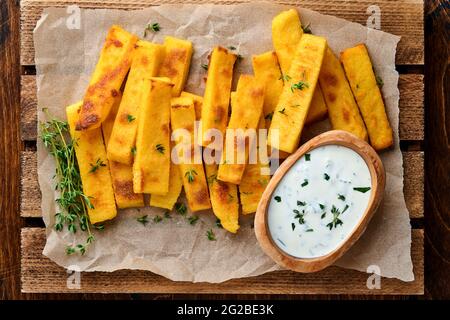 Croustilles de polenta faites maison frites avec sel de mer, parmesan, thym, romarin et sauce au yaourt. Polenta typiquement italienne. Bâtonnets de maïs frits. Dos en bois Banque D'Images