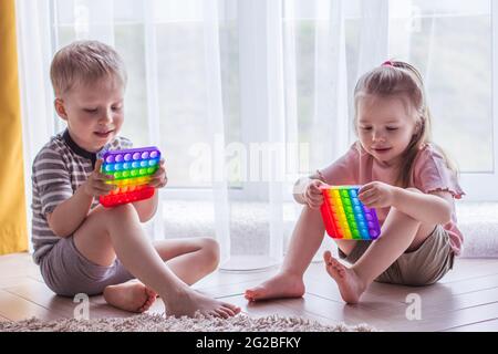 Blonde garçon et fille les enfants jouent avec le jouet sensoriel pop IT. Jeu de fidgeting de silicium tendance pour les enfants et les adultes stressés. Jouets à bulles souples et accroupés. Enfant p Banque D'Images