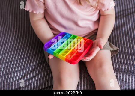 Une petite fille s'assoit et tient un jouet dans ses mains Rainbow pop il jouet de violon. Pousser Bubble fidget jouet sensoriel silicone soulagement de stress jouet. Jouet antistress FO Banque D'Images