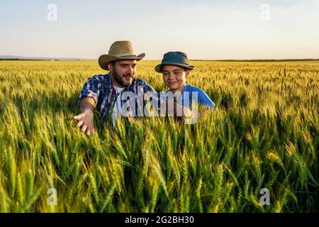 Le père et le fils sont debout dans leur champ de blé en pleine croissance. Père enseigne à son successeur l'agriculture. Banque D'Images