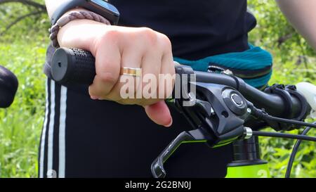 Main de femme avec anneau sur le guidon d'un VTT dans le parc de près. Le cycliste s'appuie sur le guidon du vélo Banque D'Images