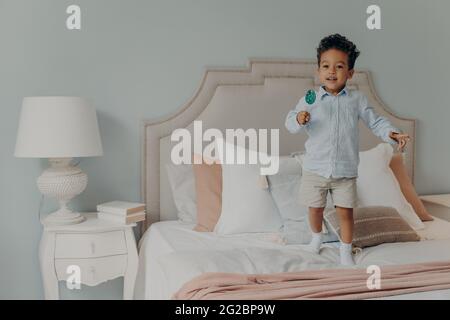 Enfant afro-américain mignon et insouciant avec lit de saut à la maison Banque D'Images