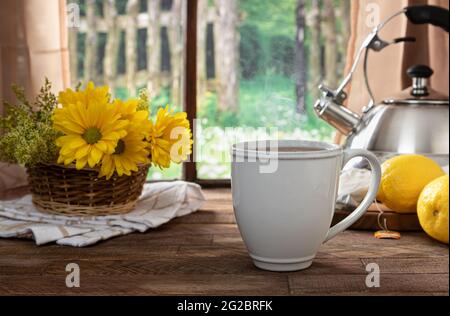 Une tasse de thé avec des citrons et des fleurs sur une table rustique en bois près d'une fenêtre à l'arrière-plan rural Banque D'Images