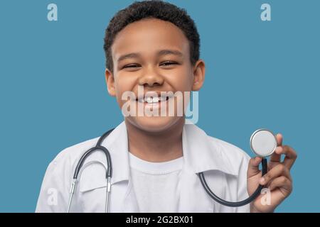 Joyeux garçon à la peau sombre montrant un stéthoscope médical Banque D'Images