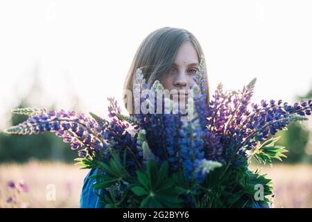 Jeune belle femme tient un grand bouquet de lupins violets dans un champ de floraison. Fleurs lupin. Écologique. Concept de la nature. Banque D'Images