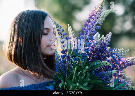 Jeune belle femme tient un grand bouquet de lupins violets dans un champ de floraison. Fleurs lupin. Écologique. Concept de la nature. Banque D'Images