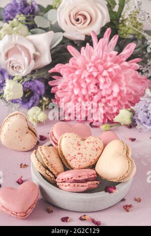 Macarons doux en forme de coeur et fleurs dans des couleurs pastel sur fond rose. Un délicieux dessert ou un cadeau pour la Saint-Valentin ou la fête des mères. VERTIC Banque D'Images