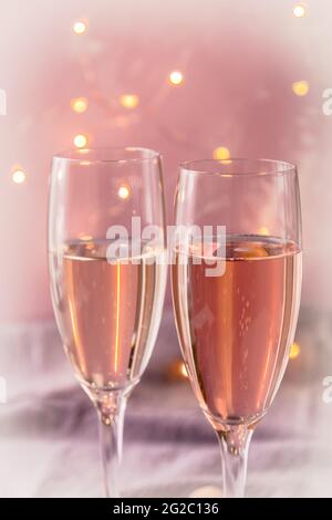 Deux verres de vin mousseux sur fond rose pastel avec lumières de fée dans une atmosphère romantique Banque D'Images